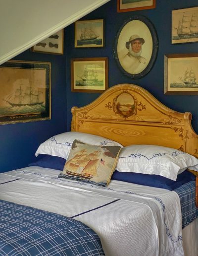Victorian painted cottage style bed with ship art gallery wall in a coastal Maine cottage.