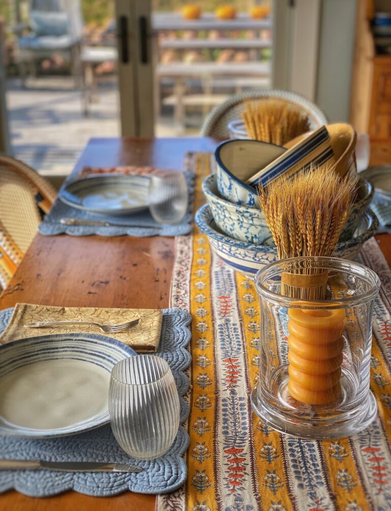 Coastal Maine Thanksgiving table setting with vintage blue and white pottery, a wheat bundle, autumn linens, and a glowing beeswax candle centerpiece.