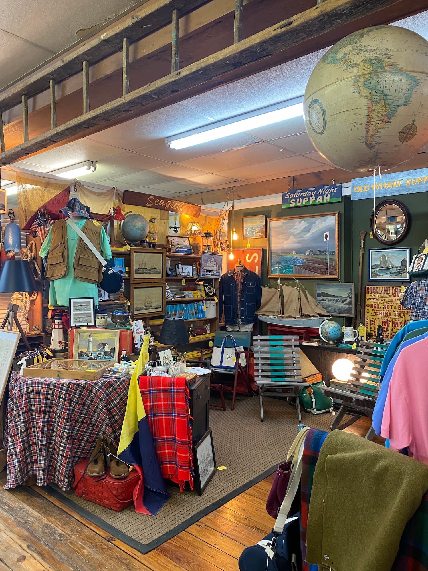 A booth at a Midcoast Maine antiques store full of nautical themed antiques, including sailing ship prints, plaid blankets, buoys, and globes.