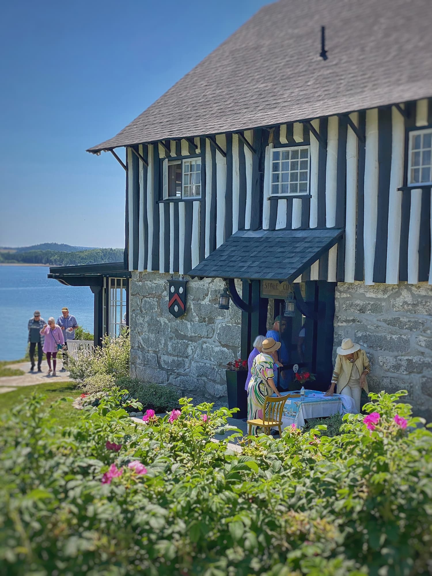 Exterior of a historic stone and half-timbered home overlooking Penobscot Bay during the Castine House & Garden Tour in Castine, Maine, with blooming rugosa roses in the foreground.